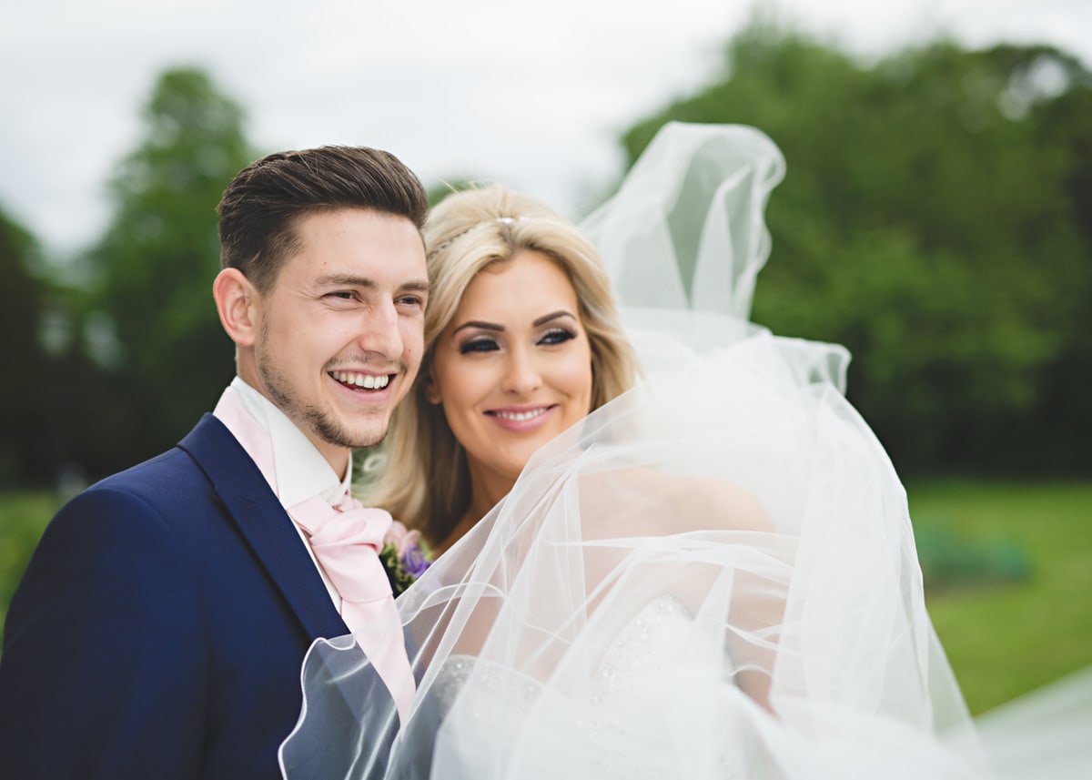 a bride and groom smiling as her veil blows in the wind
