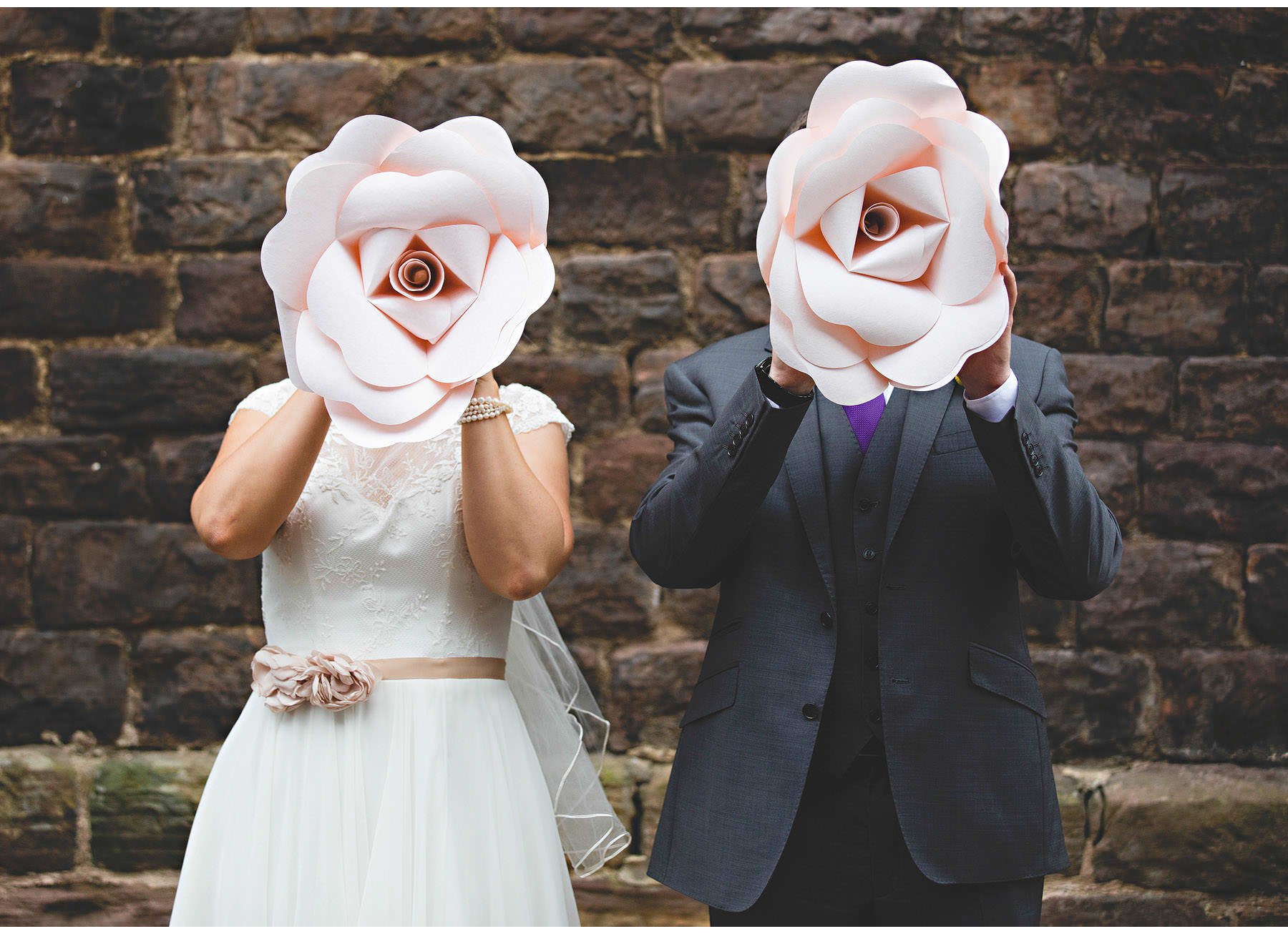 The bride & groom hiding behind giant paper flowers