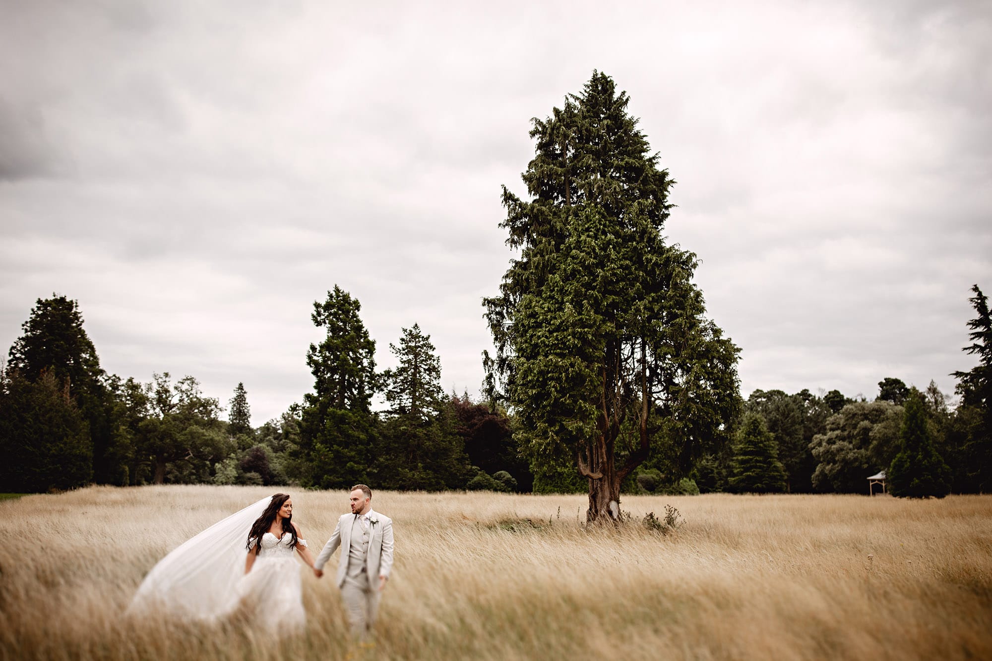 A couple's beautiful wedding photography at Hedsor House includes the newlyweds walking through a field of tall grass.